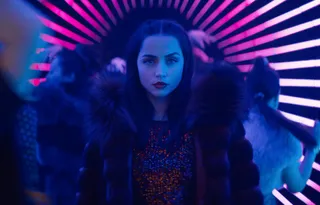 ana de armas walks through a blue and pink lit club wearing a fur coat in the movie ballerina