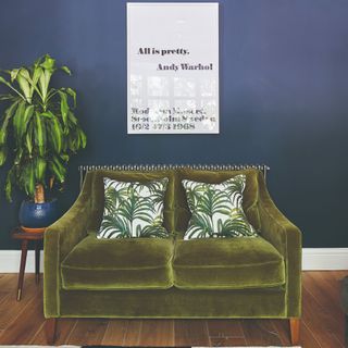 A blue-painted living room with a green velvet 2-seater sofa with two palm-print cushions