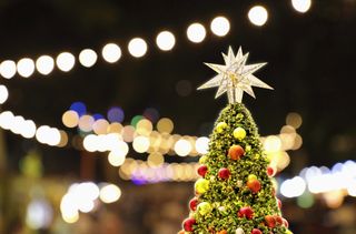 A close up of a large, star Christmas tree topper in a city square at night time.