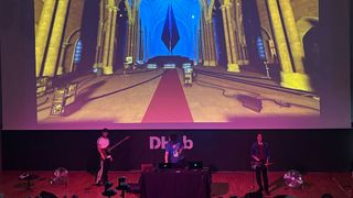 A 3 piece band playing in from of a large digital screen