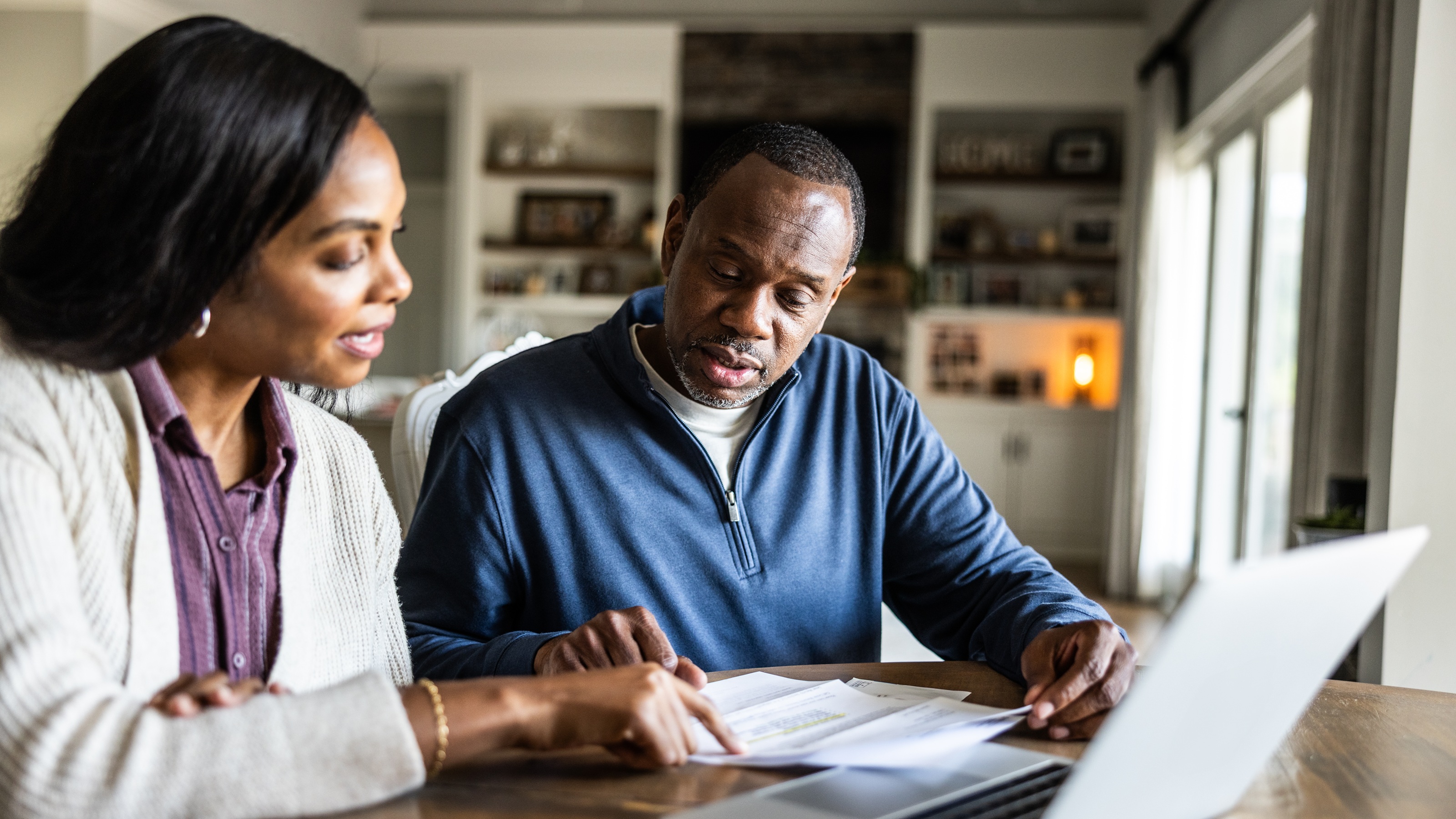 A couple discuss finances with paperwork at their dining room table.