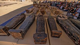 Sarcophagi found in a cache dating to the Egyptian Late Period (around the fifth century BC). In the photo we can make out about 30 sarcophaguses laid out in four rows. They are underneath a massive tend are surround by a huge crowd of people taking photos.