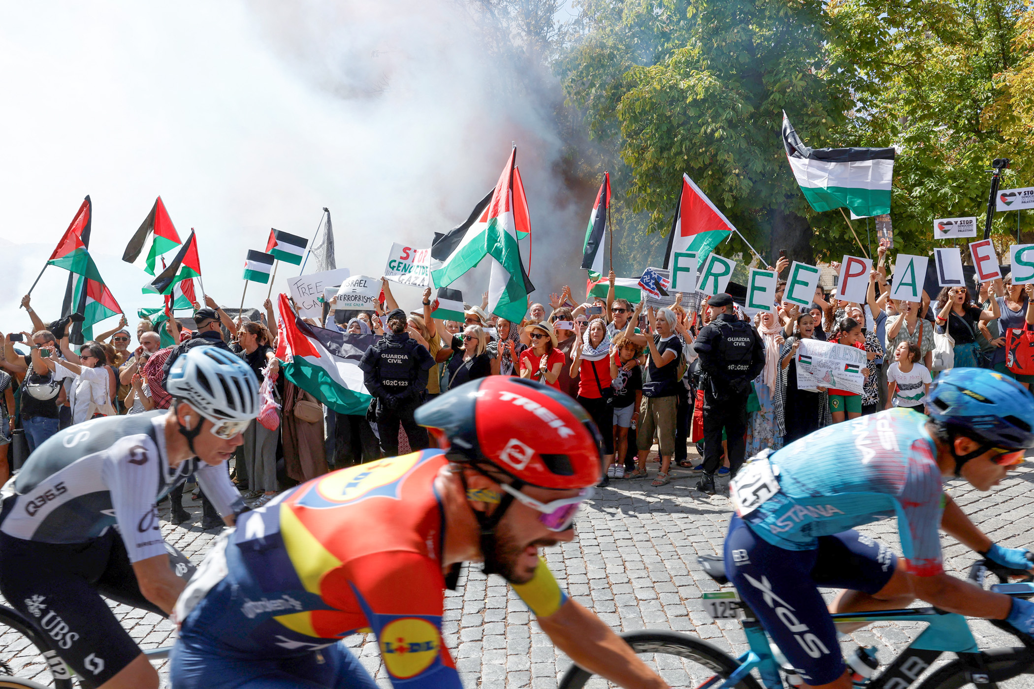 TOPSHOT - The pack rides as Pro-Palestinians protesters hold Palestinian flags during the 20th stage of the Vuelta a Espana 2025, a 156 km race between Robledo de Chavela and Bola del Mundo, in El Escorial, on September 13, 2025. (Photo by Pierre-Philippe MARCOU / AFP) (Photo by PIERRE-PHILIPPE MARCOU/AFP via Getty Images)