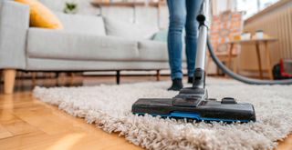 person vacuuming a deep pile rug to show how to avoid a common spring cleaning mistake when dusting