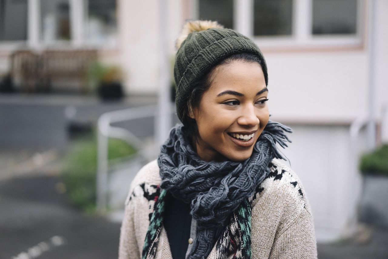 Smiling young woman wearing wooly hat outdoors, winter skin