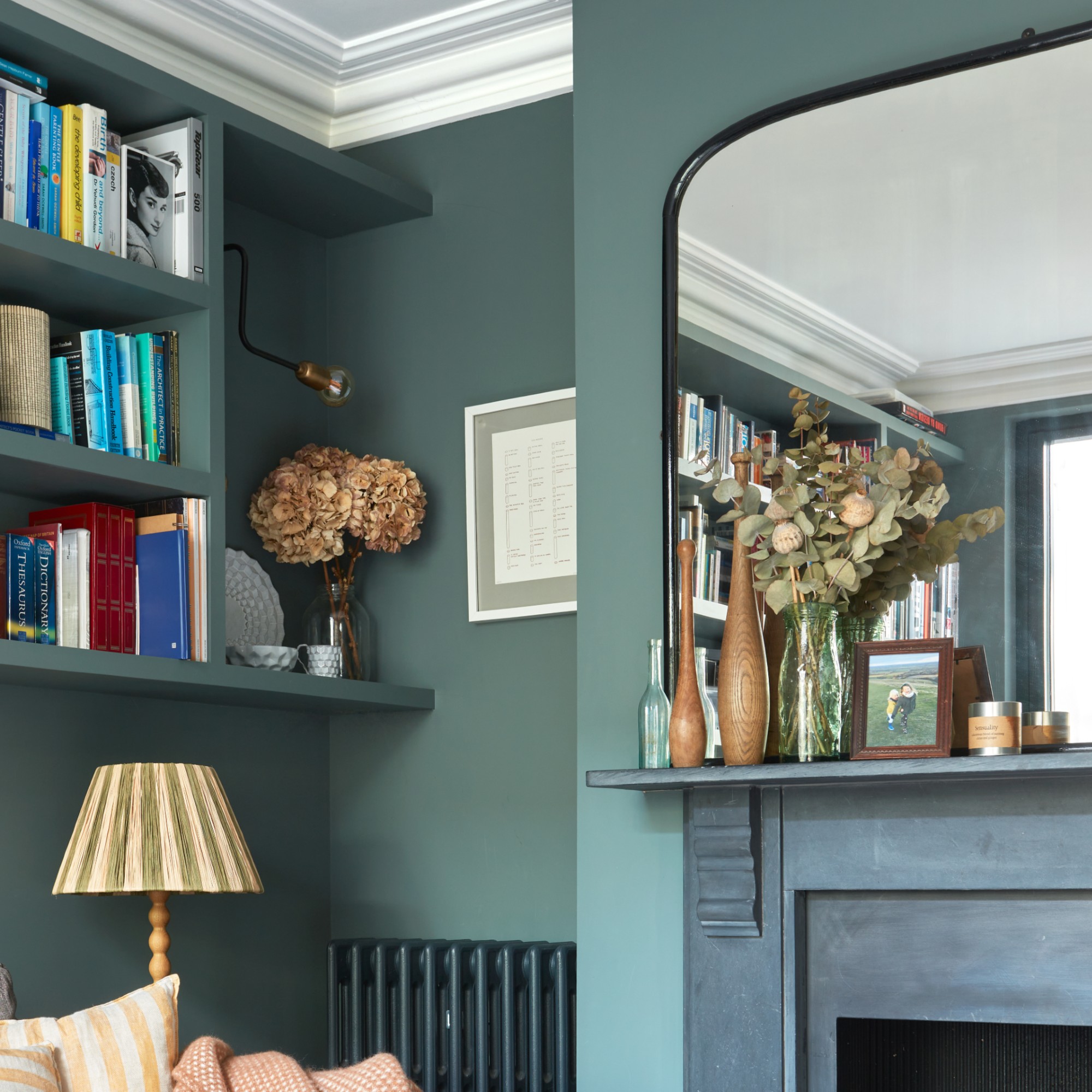 A green-painted living room with a small art work hung in the corner and a wall light pointed at it to illuminate it