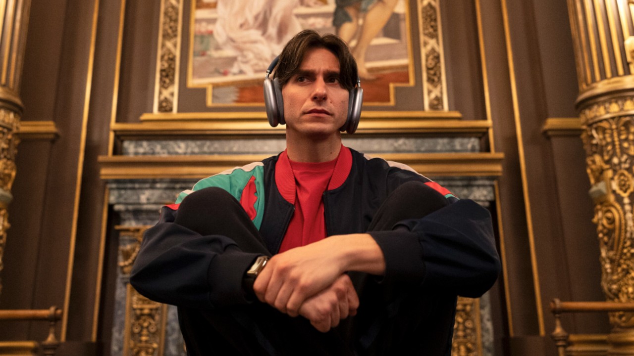 Gideon Glick sitting criss cross with his hands linked in front of him. He's wearing headphones.