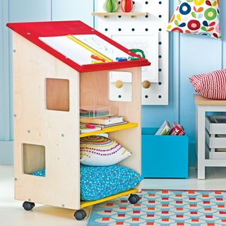 Colourful play area in a kids bedroom with house-shaped storage unit on wheels and blue walls