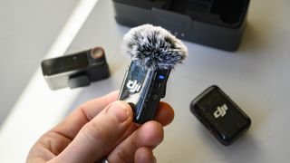 DJI Mic 2 transmitter in the hand with wind shield attached