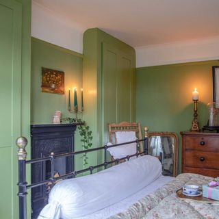 vintage bedroom with green walls and wardrobes, cast iron bed and salvaged fireplace