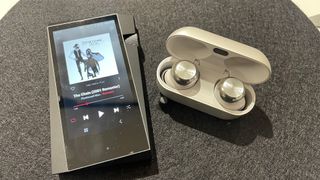 Technics EAH-AZ100 wireless earbuds in case next to music player on grey surface