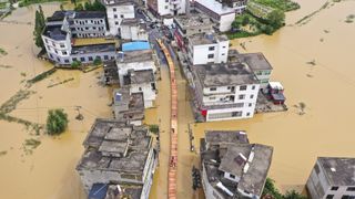 an aerial photograph shows a street of buildings all submerged in water and a central walkway build above the floodwaters in the center, people are walking along it.