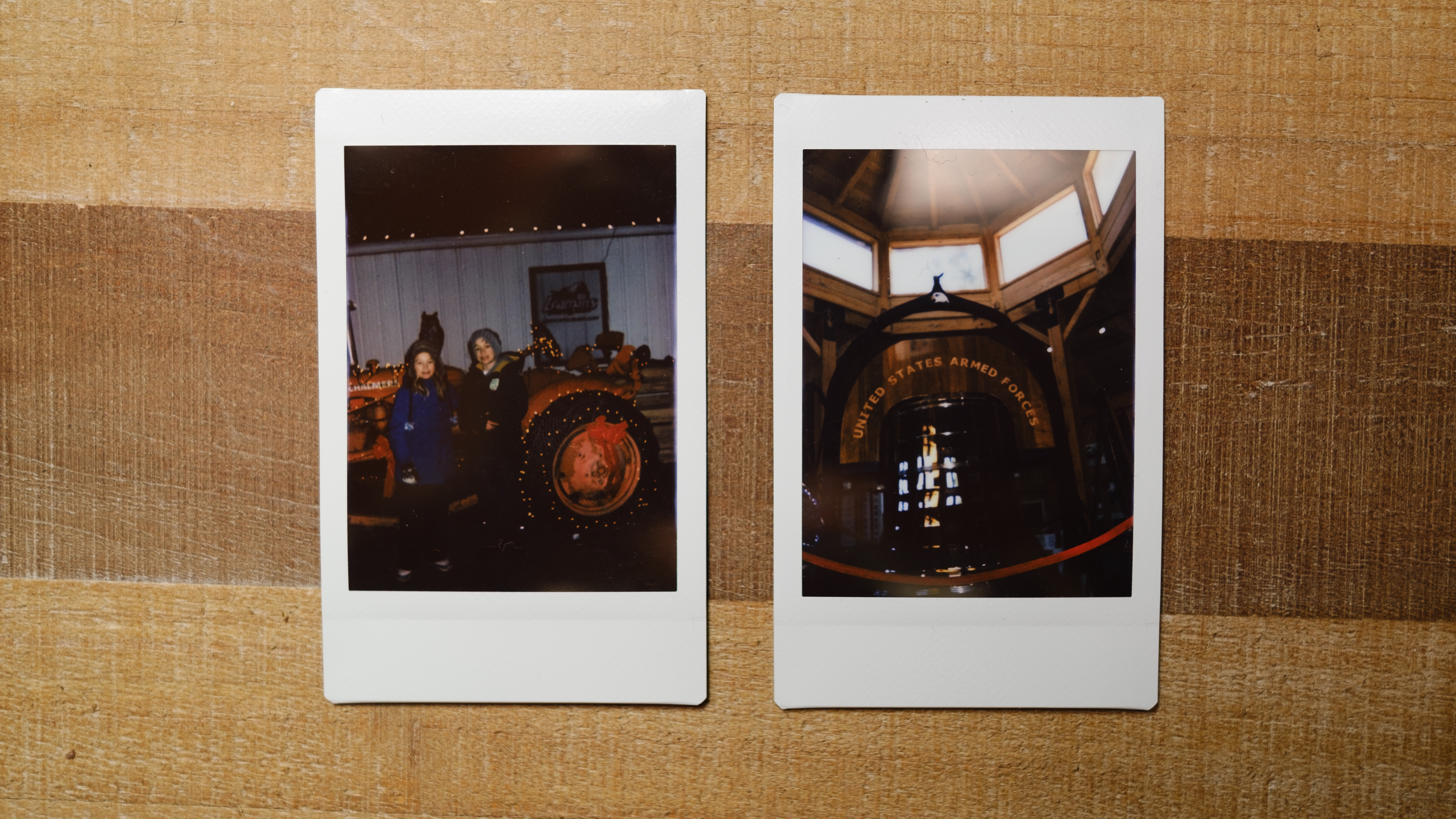 Two images from the Instax Mini SE sit on a table, one of a tractor at night and one of a large bell memorial indoors