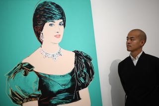 A man wearing a black suit looking at a turquoise painting of Princess Diana by Andy Warhol