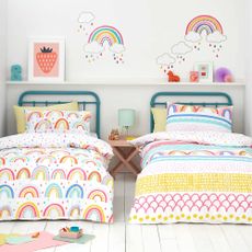 A white bedroom with two single childrens beds both with bright rainbow coloured bedding