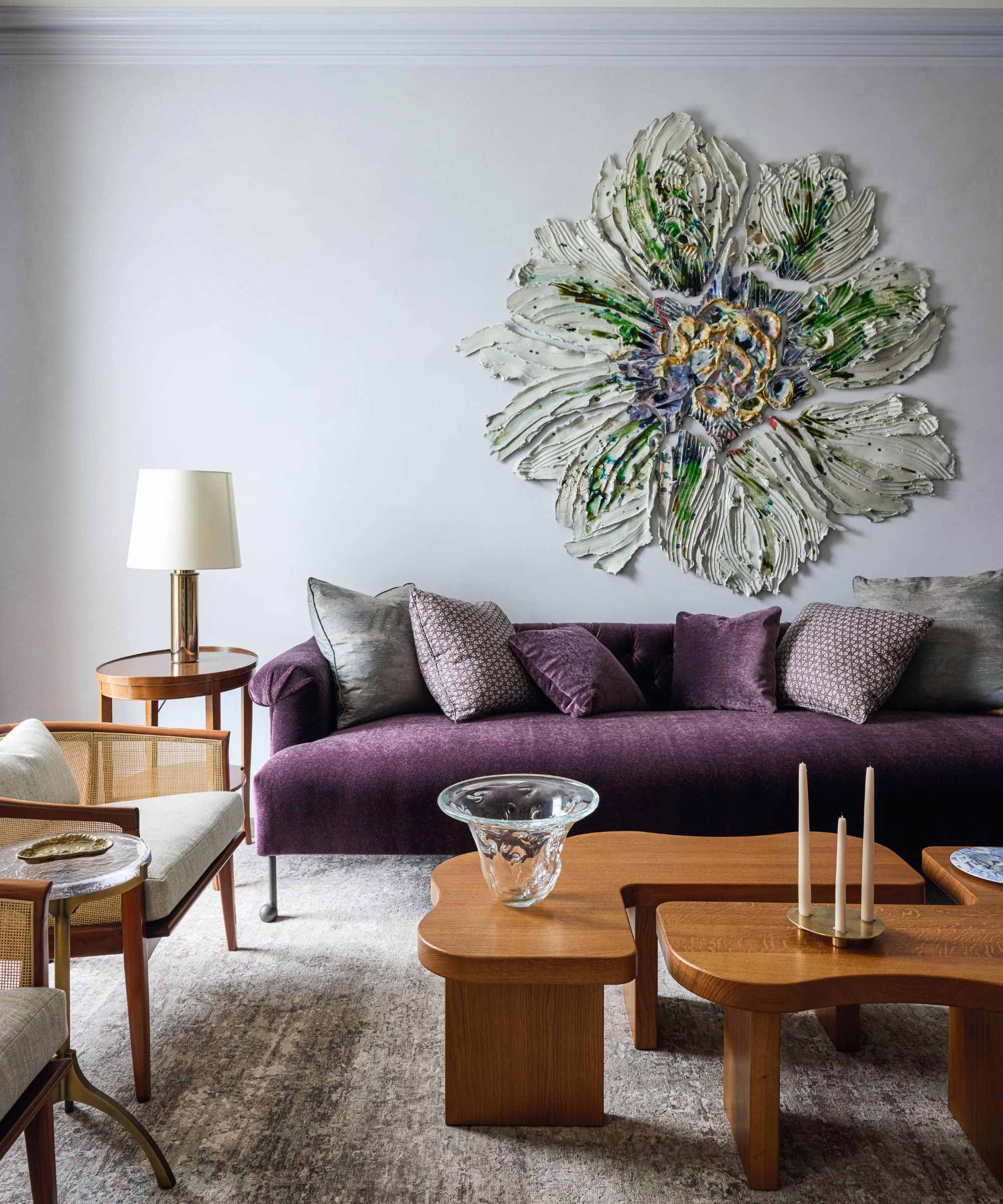 a light blue painted sitting room with a large abstract painted flower installation on the wall above a purple couch