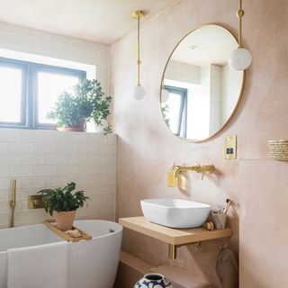 Bathroom with plaster walls, and large gold round mirror above a wooden vanity unit