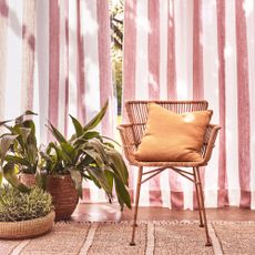 A rattan open back chair next to houseplants in front of airy curtains