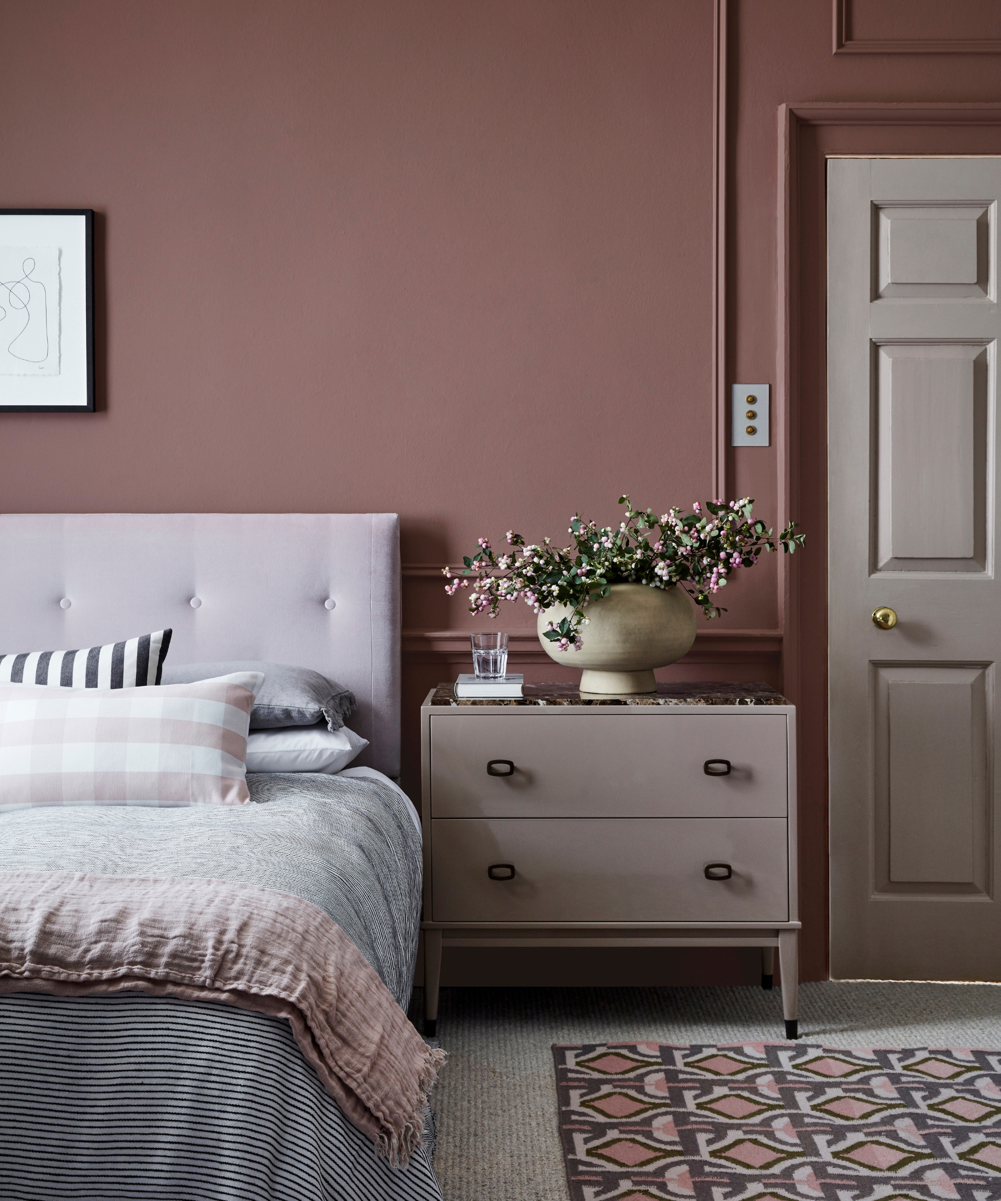 Bedroom with dusky mauve walls, soft pink bedding, gray textiles, a taupe dresser, and a patterned rug in muted blush tones.