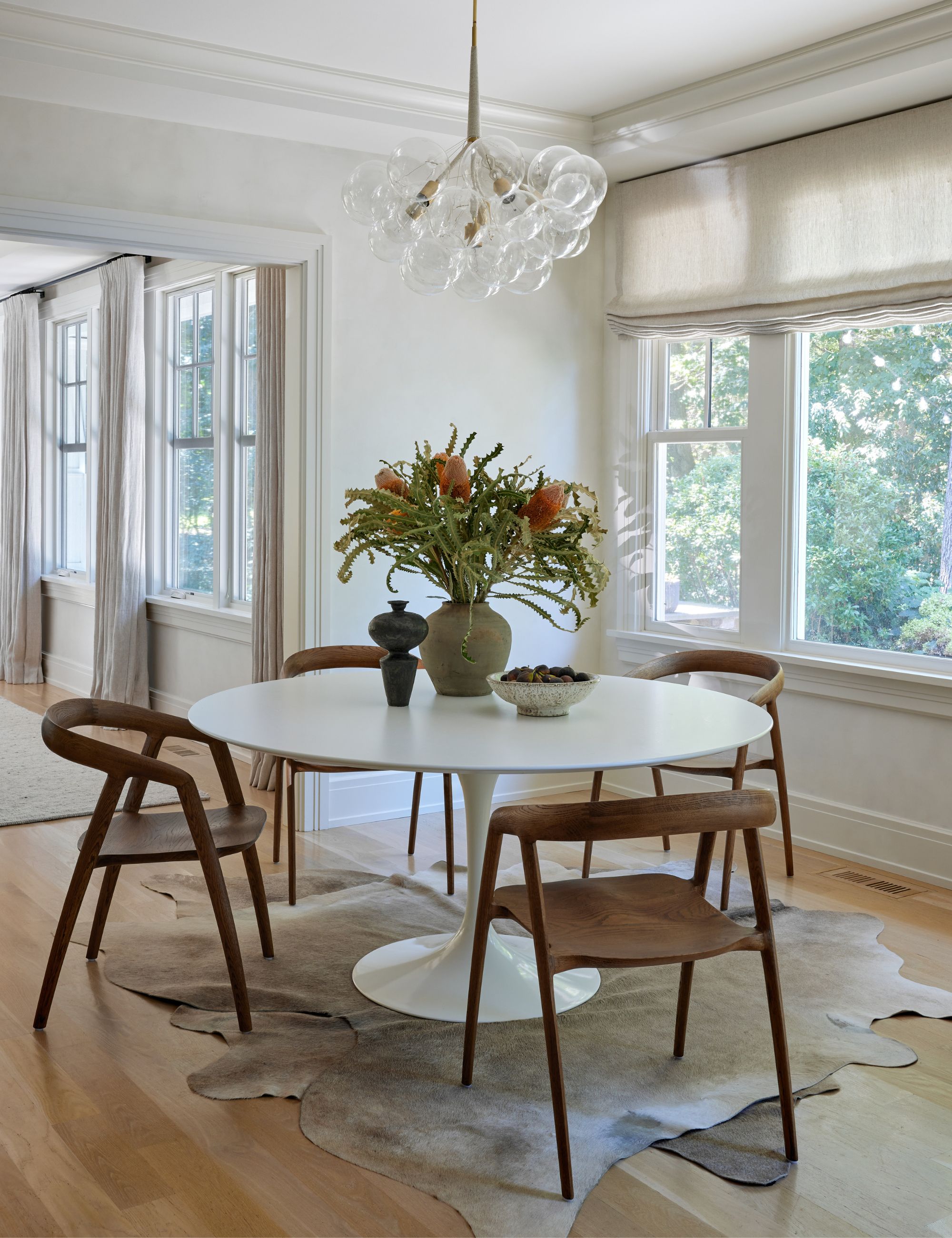 Modern home with large windows, blinds, round table, wooden chairs and two rugs placed underneath each other on the floor.