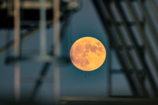 A full moon is seen rising between industrial metal railings ang guards.