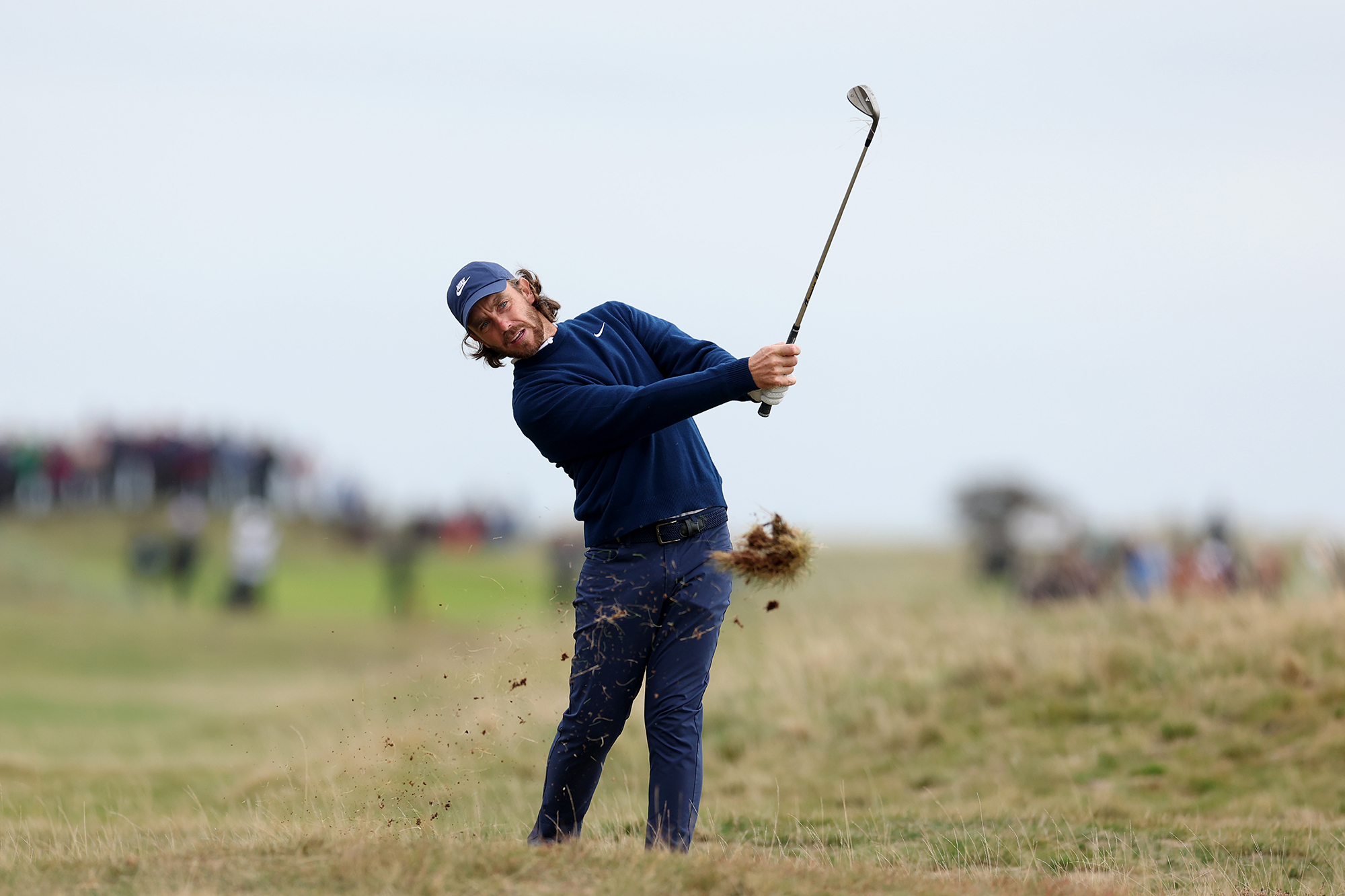 Tommy Fleetwood in the finish position with a wedge as a divot flys up following contact with the ground