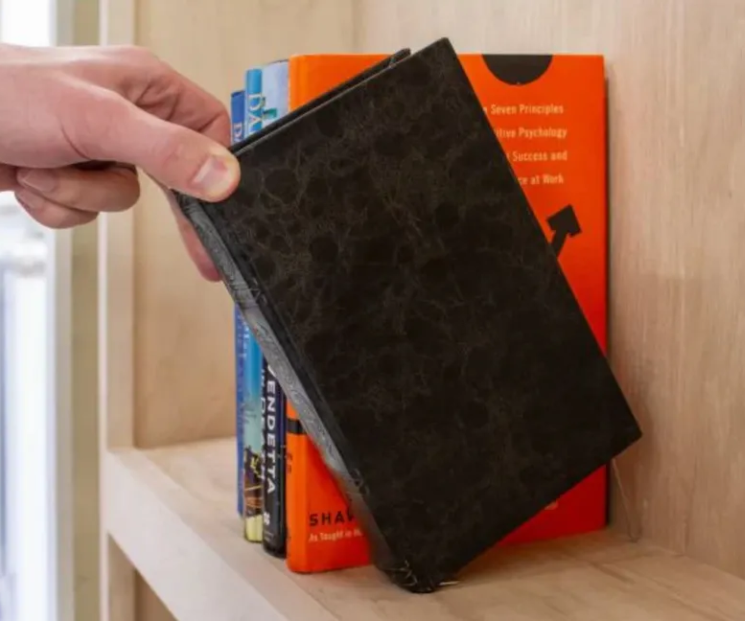 Hand pulling a book from a wooden shelf