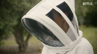 Meghan Markle wearing a white beekepers hat standing in front of a tree