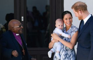 Archbishop Desmond Tutu laughing as he looks at Prince Harry and Meghan Markle holding baby Prince Archie in front of a doorway