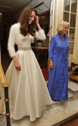 Kate Middleton wearing a white ballgown for her wedding reception standing next to Queen Camilla wearing a blue dress