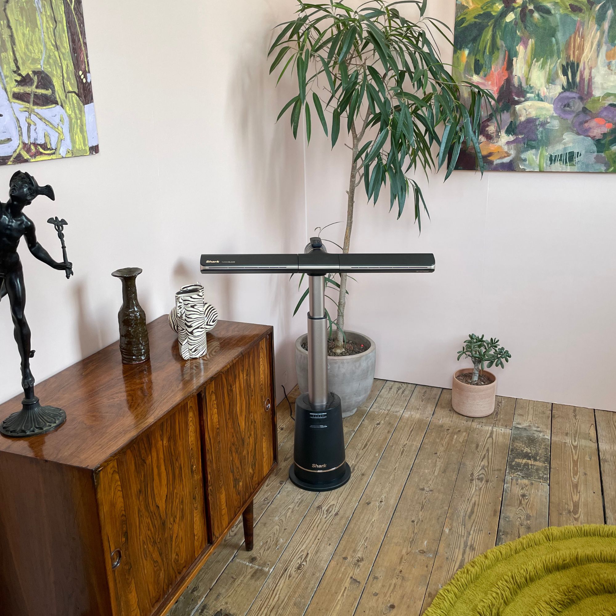 Shark TurboBlade fan in a light pink room, surrounded by furniture and a plant behind it