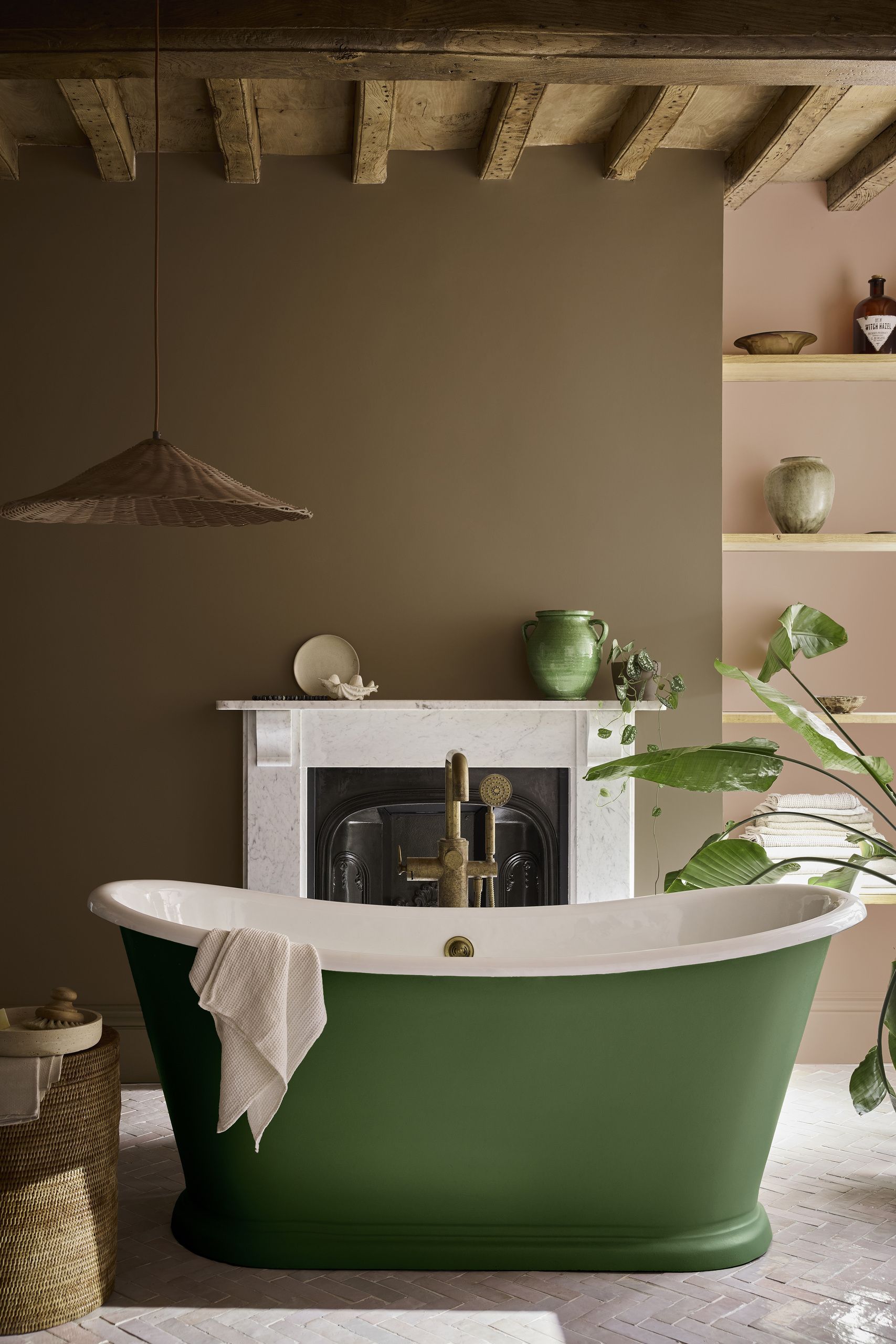 Image of a bathroom with brown and light pink walls, a green bathtub, a marble fireplace, and rattan decor.
