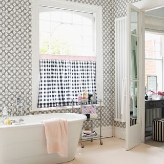 chic monochrome bathroom with graphic print wallpaper gingham curtain freestanding white bath and glass shelving on wheels