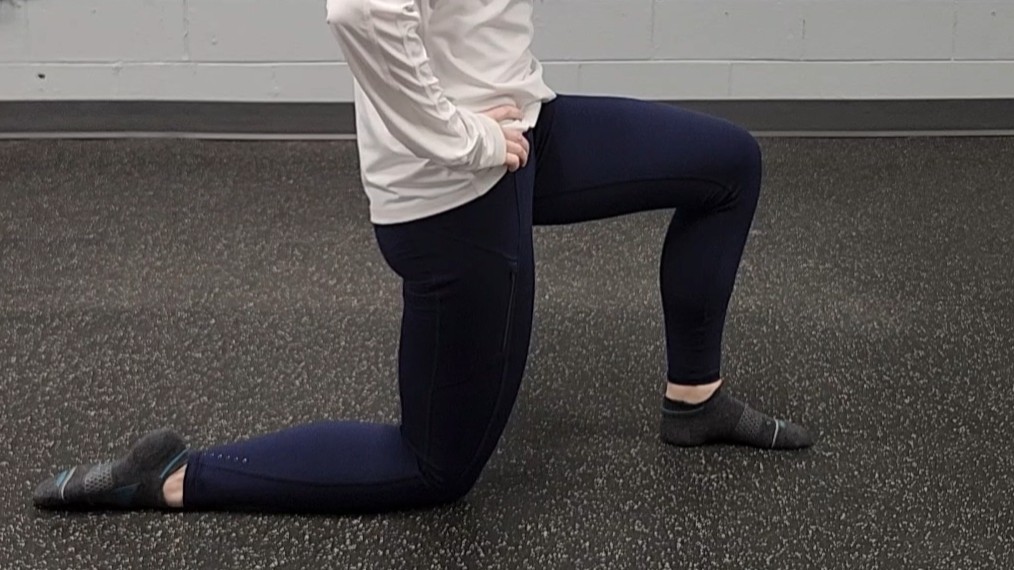 Woman demonstrating stretch. She wears a white long-sleeve top, blue sports leggings and black socks