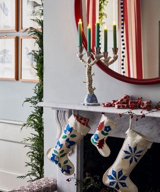 Christmas stockings hanging from a mantelpiece with lit candles in a candlestick in front of the mirror.