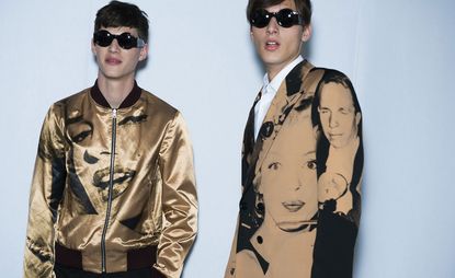 Two male models wearing clothing with faces on by Dries Van Noten in brown and black.