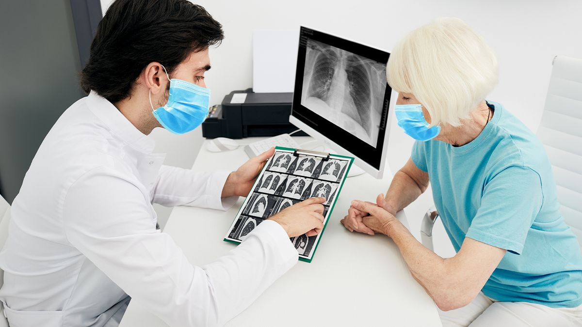 Pulmonologist wearing a surgical mask showing a senior patient a CT scan of her lungs