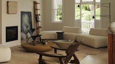 Image of a white/beige living room with mid-century furniture mixed with contemporary furniture. There is a long and low, curved sofa, two stone coffee tables, wooden accent chairs and a black floor lamp.