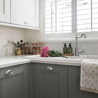 Kitchen sink underneath a window in a kitchen with grey cabinets and a speckled white worktop