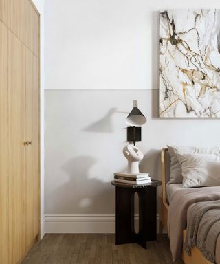 Corner of small bedroom space with small side table and sculptural table lamp on show, accented by white walls and marbled wall art