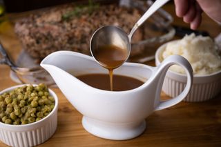 Close up of a gravy boat with gravy being scooped with a ladel