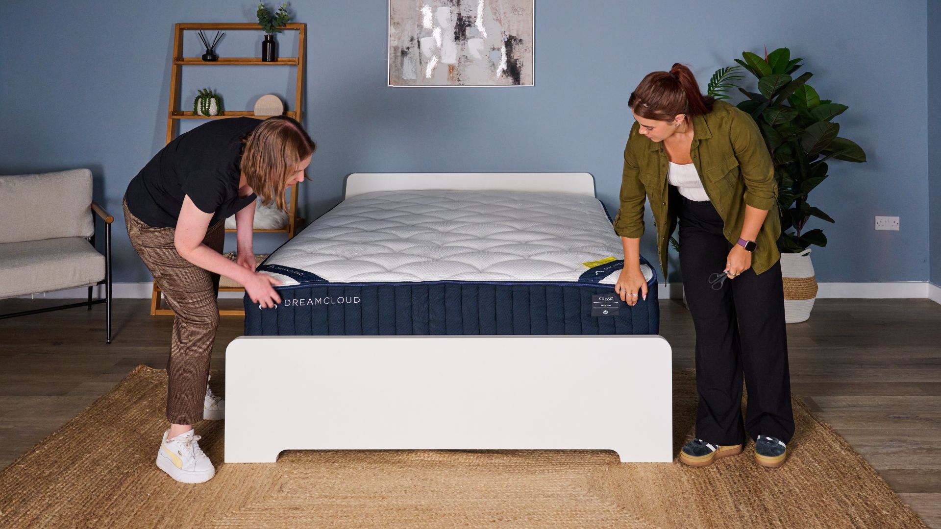 Two testers inspect the edges of the newly unboxed DreamCloud Classic mattress in a blue bedroom.