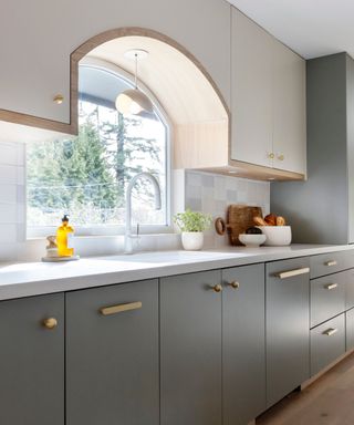 A blue, white, and wood kitchen with curved profiles and gold hardware and a large window behind the sink