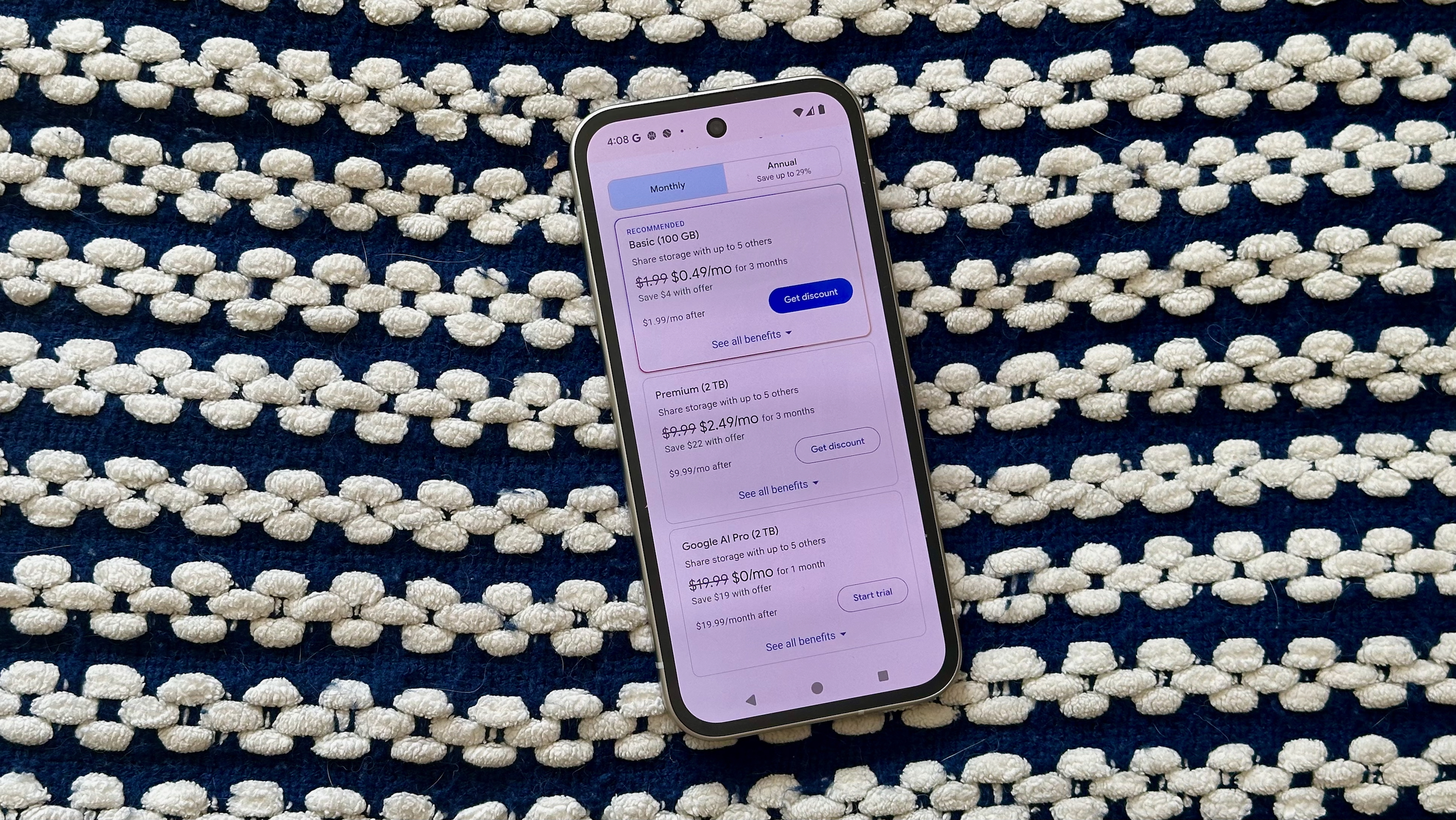 A Pixel 9a sitting on a blanket showing Google One Basic, Premium, and AI Pro plan options.