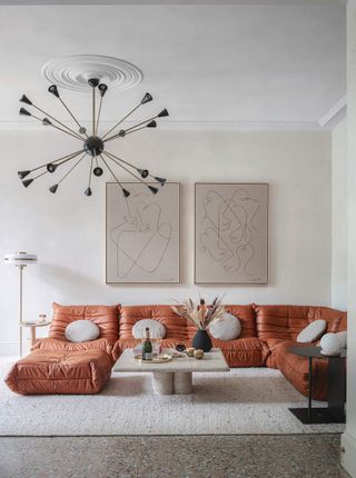 A living room with a large l-shaped orange sofa, tall ceilings and a statement pendant light