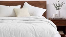 White Pure Down blanket on a dark wood bedframe with matching bedside table with books, white teacup, and white vase filled with eucalyptus