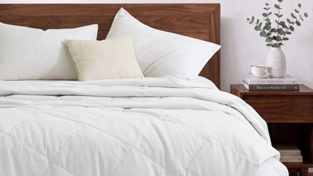 White Pure Down blanket on a dark wood bedframe with matching bedside table with books, white teacup, and white vase filled with eucalyptus
