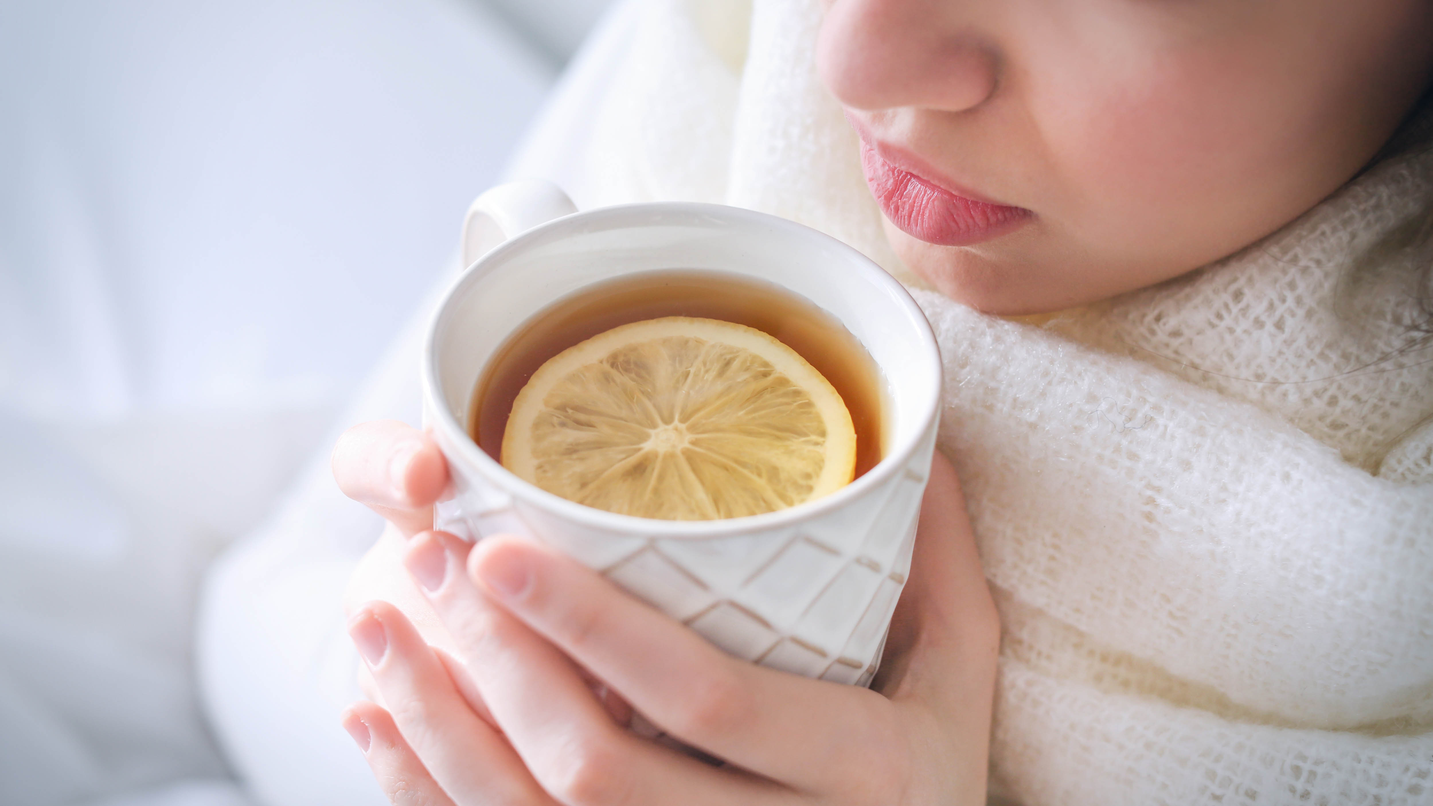 A person holding a cup of tea with a slice of lemon inside