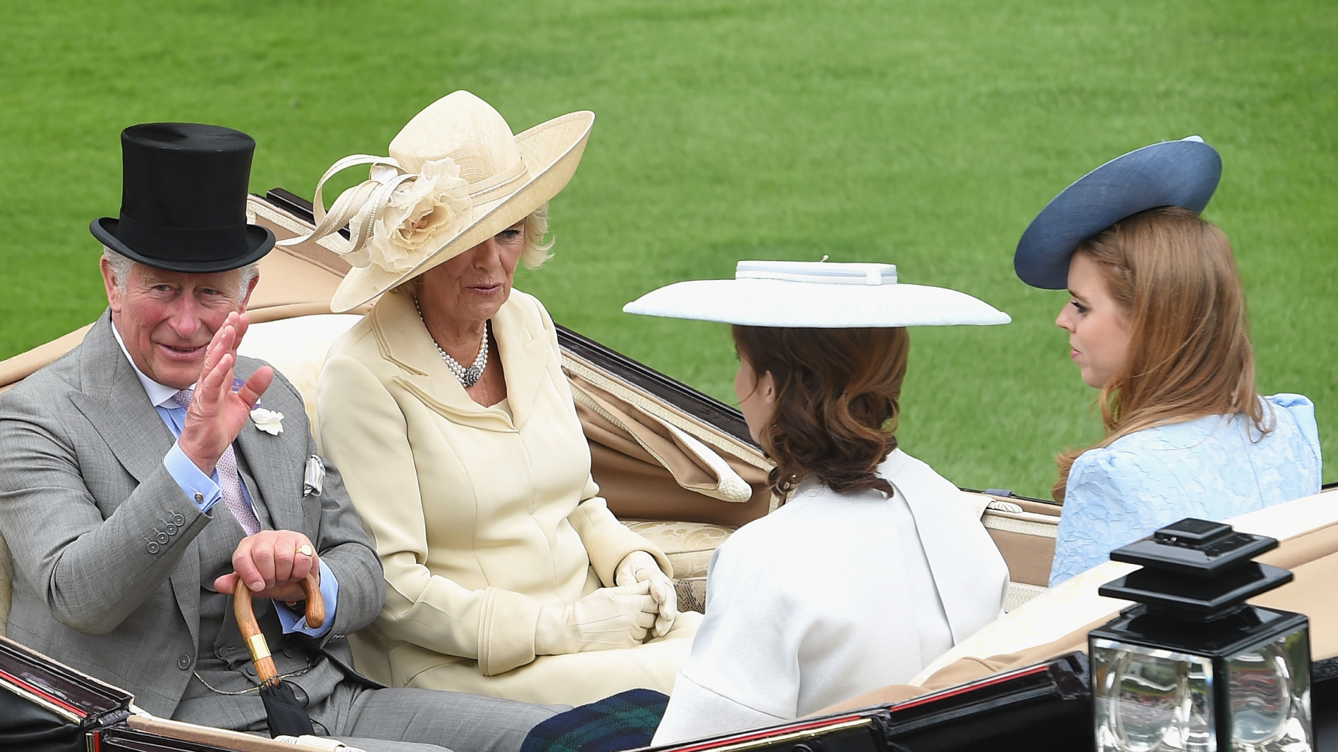 King Charles riding in a carriage waving with Queen Camilla, Princess Eugenie and Princess Beatrice