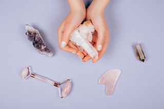 Pink facer stone massagers and gua sha in woman hands on violet background